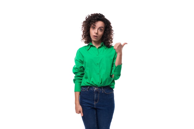 A young brunette woman with a stylish hair styling by a curly method dressed in a green shirt points