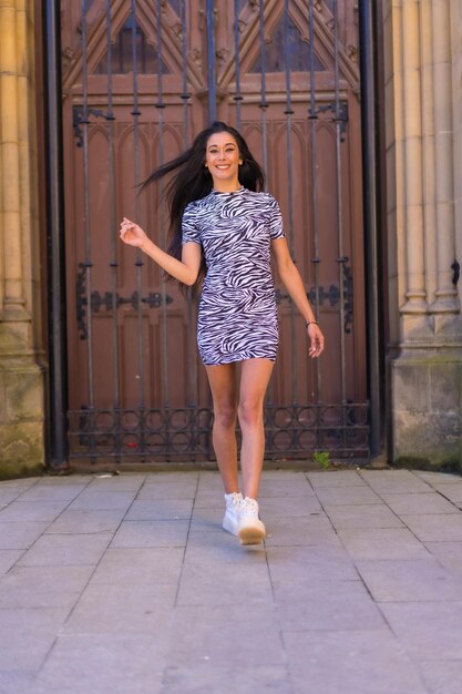 Young brunette woman in a zebra print jumpsuit smiling while visiting the city on vacation