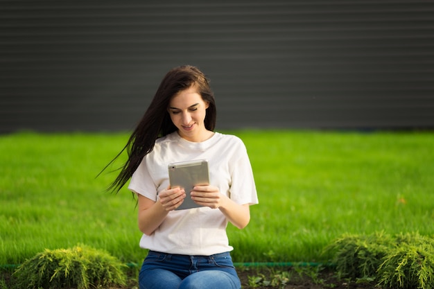 Young brunette womanwith tablet serfing in internet on grass