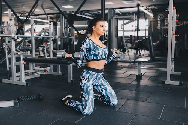 Young brunette works out with hand weights in gym. Athlete builder muscles lifestyle.