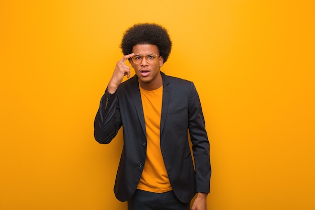 Young business african american man on an orange wall doing a disappointment gesture with finger