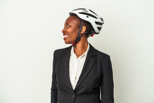 Young business african american woman wearing a bike helmet isolated on white background looks aside smiling, cheerful and pleasant.