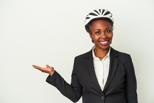 Young business african american woman wearing a bike helmet isolated on white background showing a copy space on a palm and holding another hand on waist.