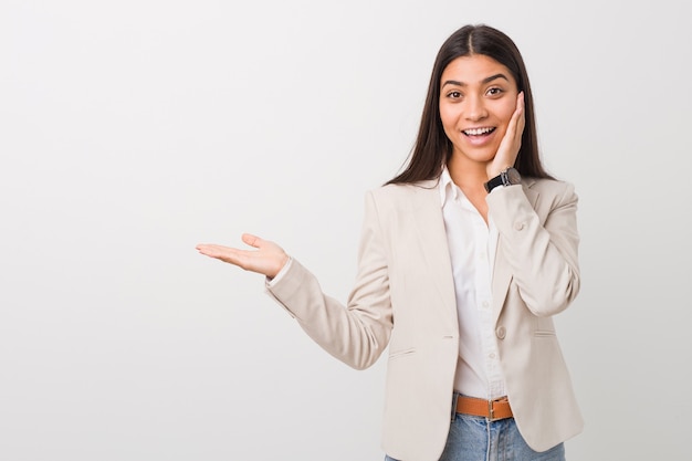 Young business arab woman isolated against a white background holds copy space on a palm, keep hand over cheek