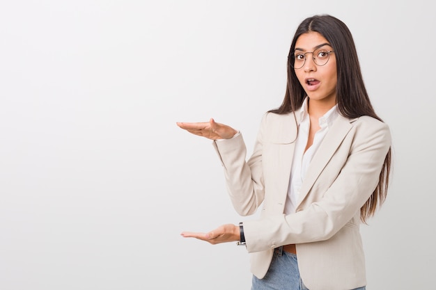 Young business arab woman isolated against a white  shocked and amazed holding a copyspace between hands.