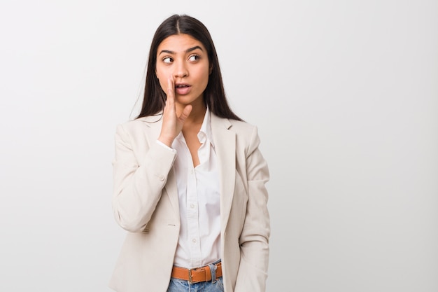 Young business arabic woman isolated against a white wall is saying a secret hot braking news and looking aside