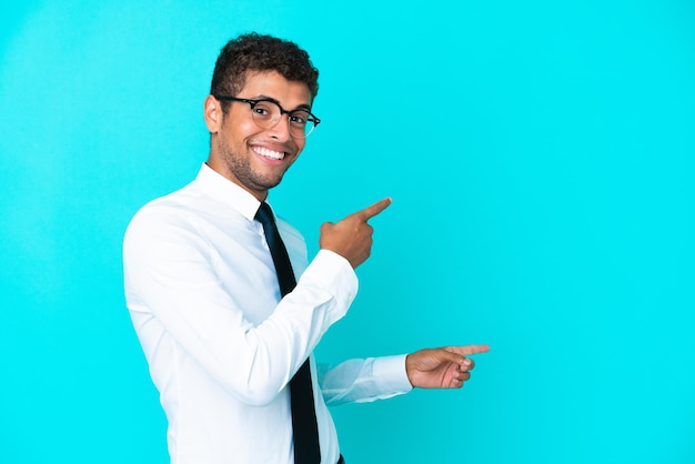 Young business Brazilian man isolated on blue background pointing finger to the side and presenting a product