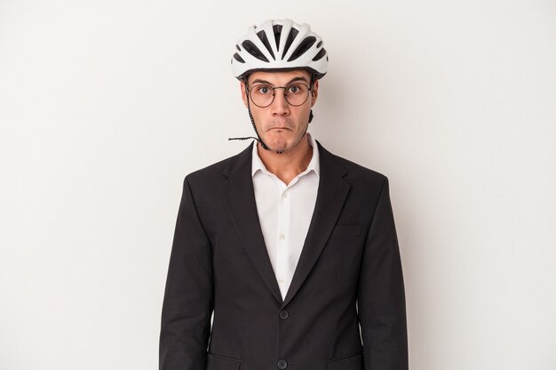 Young business caucasian man holding bike helmet isolated on white background shrugs shoulders and open eyes confused.