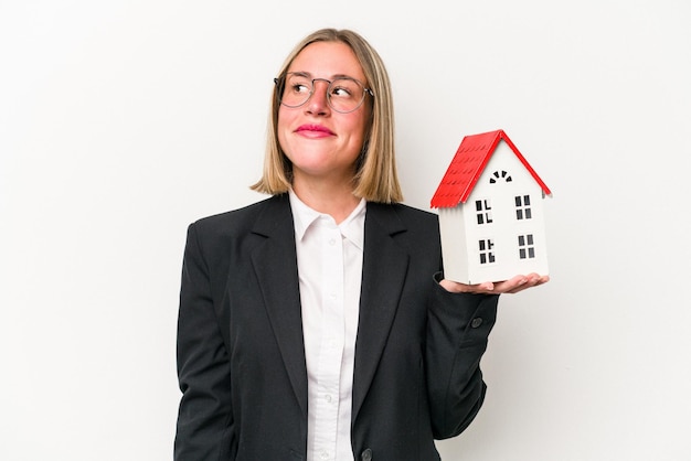 Young business caucasian woman holding a toy house isolated on white background dreaming of achieving goals and purposes