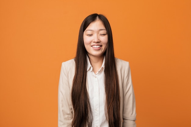 Young business chinese woman laughs and closes eyes, feels relaxed and happy.