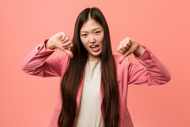 Young business chinese woman wearing pink suit showing thumb down and expressing dislike.