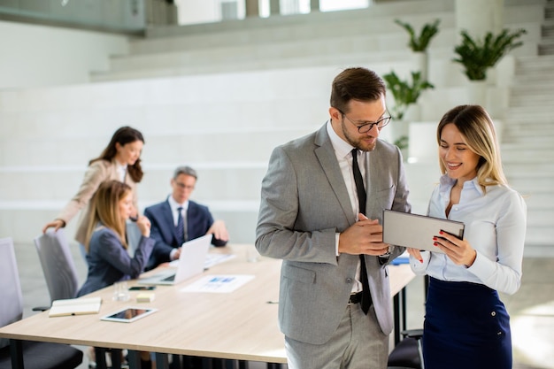 Young business couple looking at financial results on digital tablet in front of their team at the office