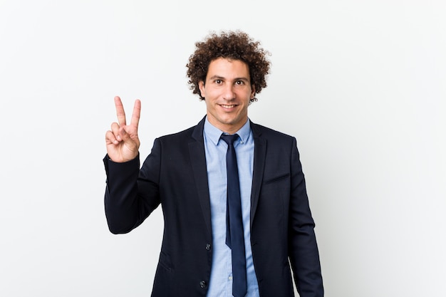 Young business curly man on white showing victory sign and smiling broadly.