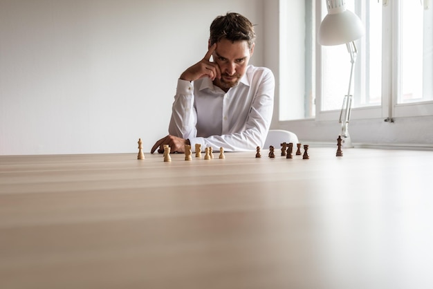 Young business executive leader siting at his desk with teams of black and white chess pieces on hiss office desk making hr decisions.