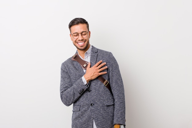 Young business filipino man against a white wall laughs out loudly keeping hand on chest.