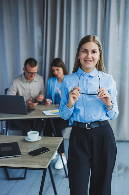 Young business lady Manager woman in classic glasses smiling during working time in office desk with laptop colleagues in background A colleague is in the background selective focus