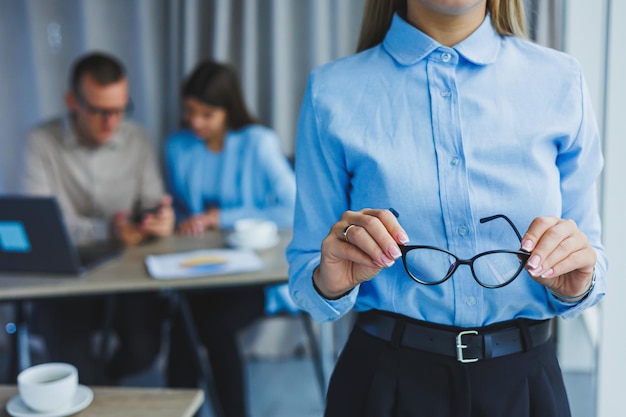 Young business lady Manager woman in classic glasses smiling during working time in office desk with laptop colleagues in background A colleague is in the background selective focus