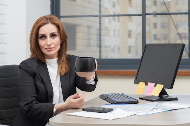 Young business lady sitting at the office and holding coffee mug