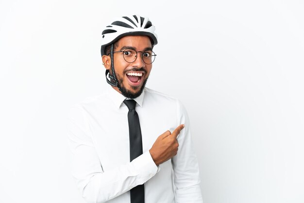 Young business latin man holding a bike helmet isolated on white background surprised and pointing side