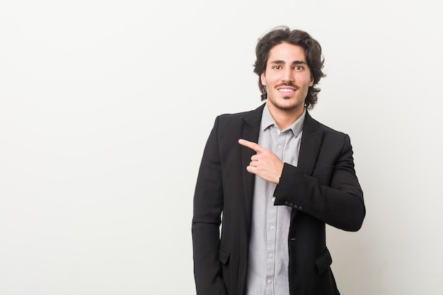 Young business man against a white smiling and pointing aside, showing something at blank space.