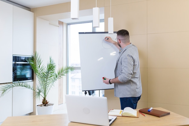 young business man in casual clothes online meeting presentation or training using a laptop webcam and a flipchart with markers