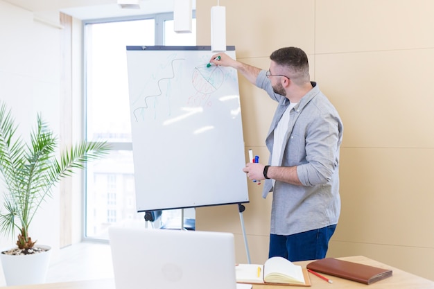 young business man in casual clothes online meeting presentation or training using a laptop webcam and a flipchart with markers