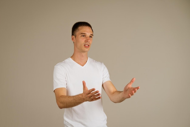 Young business man of caucasian ethnicity in a white tshirt on the background posing gesturing with ...