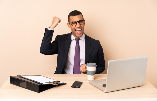 Young business man in his office with a laptop and other documents celebrating a victory