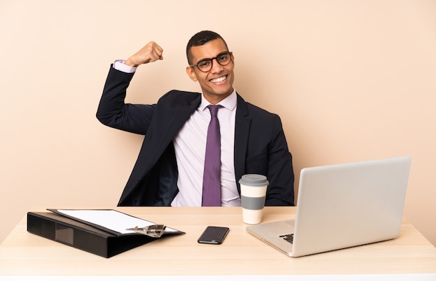 Young business man in his office with a laptop and other documents doing strong gesture