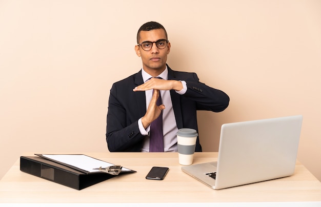 Young business man in his office with a laptop and other documents making time out gesture