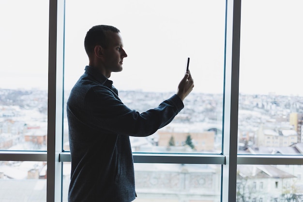 Young business man holding a phone In an office or business center against the background of large windows of a skyscraper Work and career concept