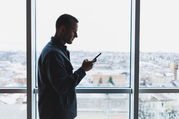 Young business man holding a phone In an office or business center against the background of large windows of a skyscraper Work and career concept