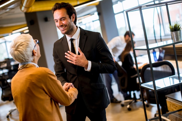 Young business man and senior business woman shaking hands in the office