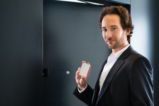 Young business man standing with a keycard in front of a room door in a hotel