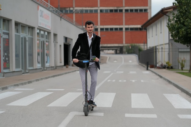 Young business man in suit driving an electric scooter to work through the city street