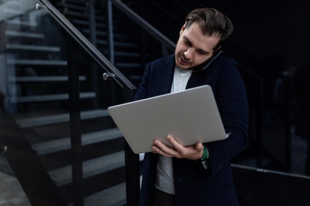 Young business man talking on the phone with a laptop in his hands outside the office