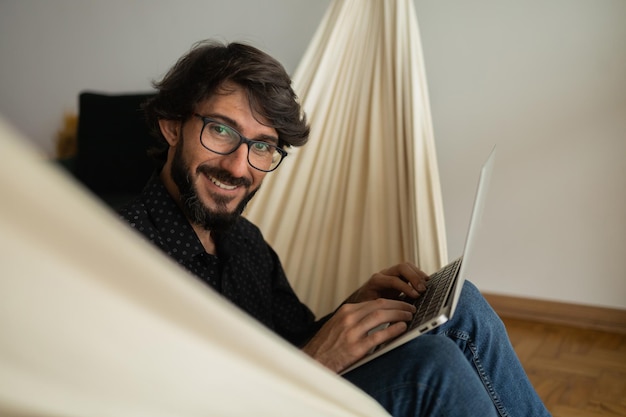 Young business man with black glasses working at home with laptop on a white hammock Gray notebook for working Home office concept High quality photo                         person