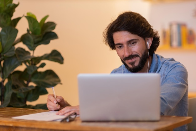 Young business man working at home with laptop and papers on desk Gray notebook for working and white headphones Home office concept High quality photo                         person