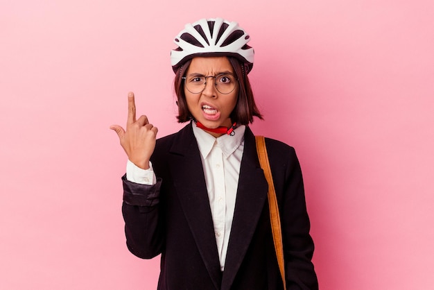 Young business mixed race woman wearing a bike helmet isolated on pink background showing a disappointment gesture with forefinger.