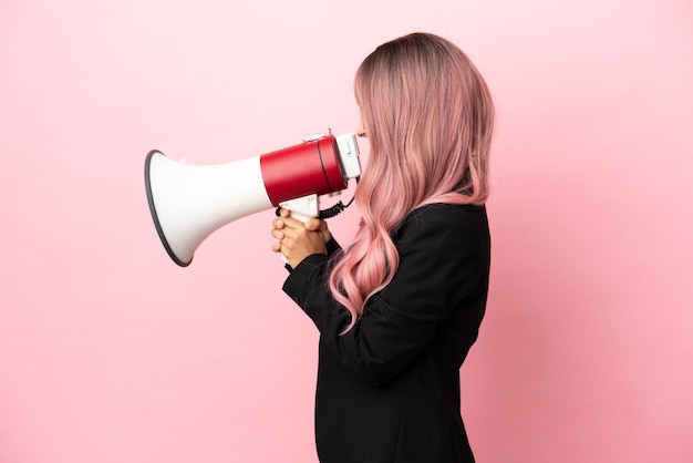 Young business mixed race woman with pink hair isolated on pink background shouting through a megaphone