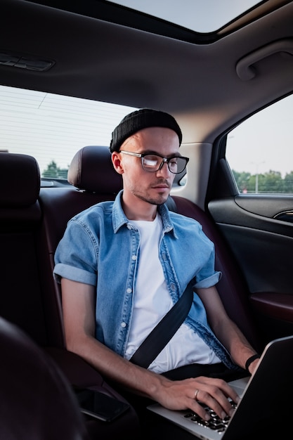 Young business person using laptop on a backseat of a car.