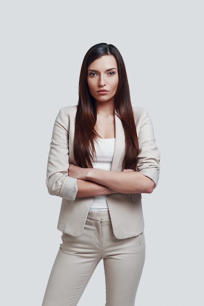 Young business professional. Attractive young woman looking at camera while standing against grey background