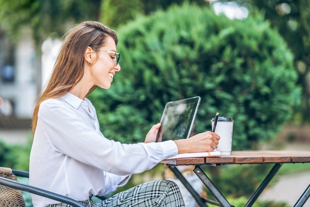 Young business woman drinking coffe and working on tablet in street cafe.