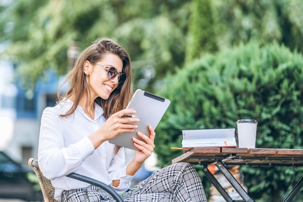 Young business woman drinking coffe and working on tablet in street cafe.