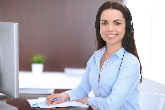 Young business woman in a headset, sitting at the table in the office.