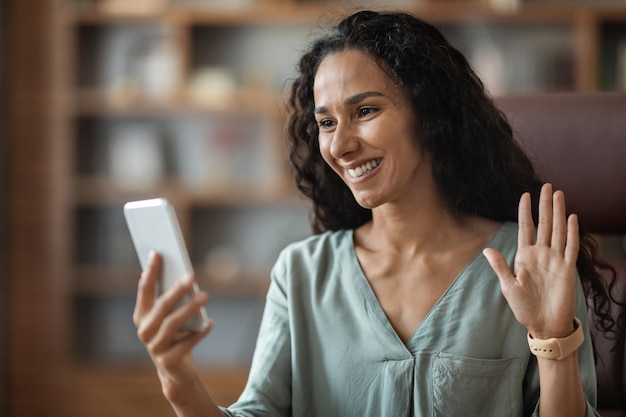 Young business woman holding phone looking at screen waving