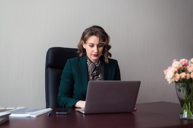 Young business woman or manager sitting at workplace with laptop