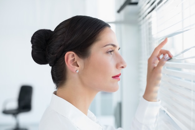 Young business woman peeking through blinds at office