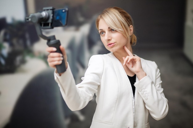 Young business woman recording video blog on smartphone in company office.