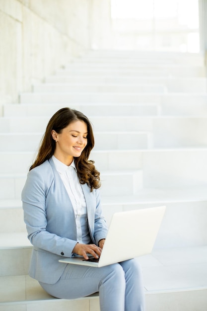 Young business woman sitting on the stairs on office hallway and working on laptop